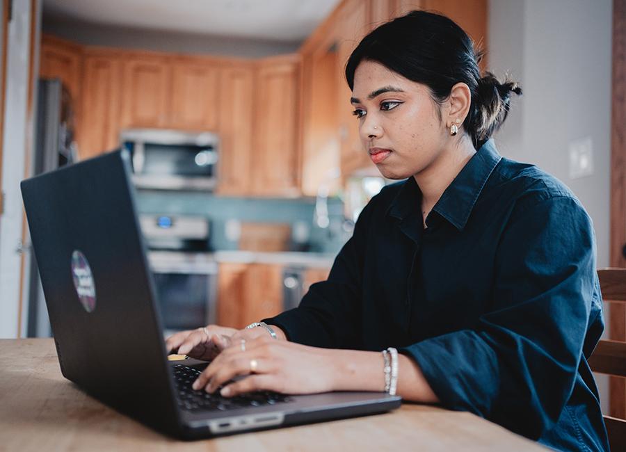 image of a female student working on her laptop in a common area completing work for an online innovation certificate