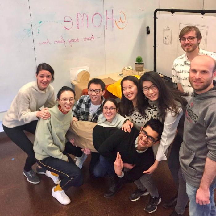 A group of students take a break from working on their Internet of Things project to smile for the camera in front of a whiteboard.